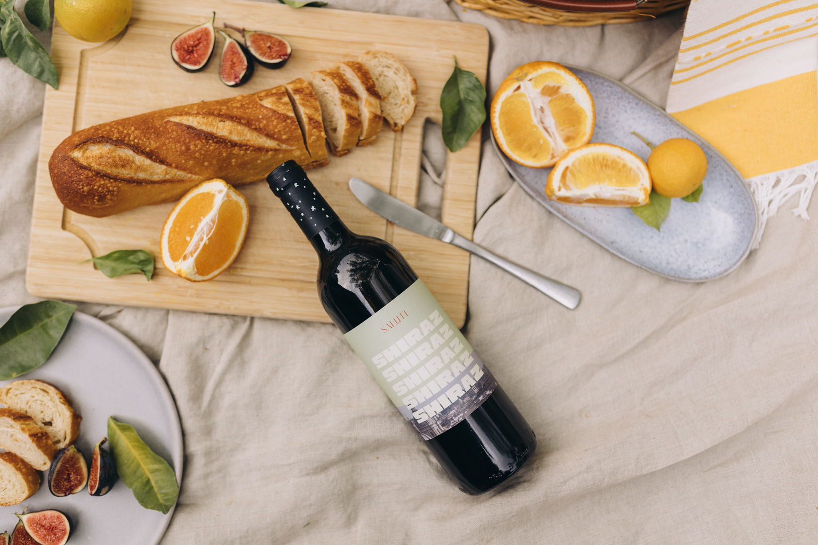 a bottle of wine, bread and fruit on a picnic blanket