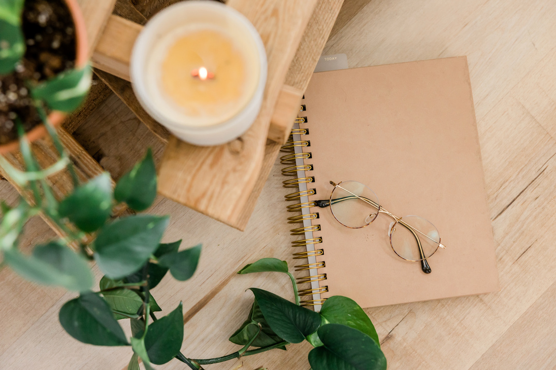 a notebook, glasses and a candle on a wooden table