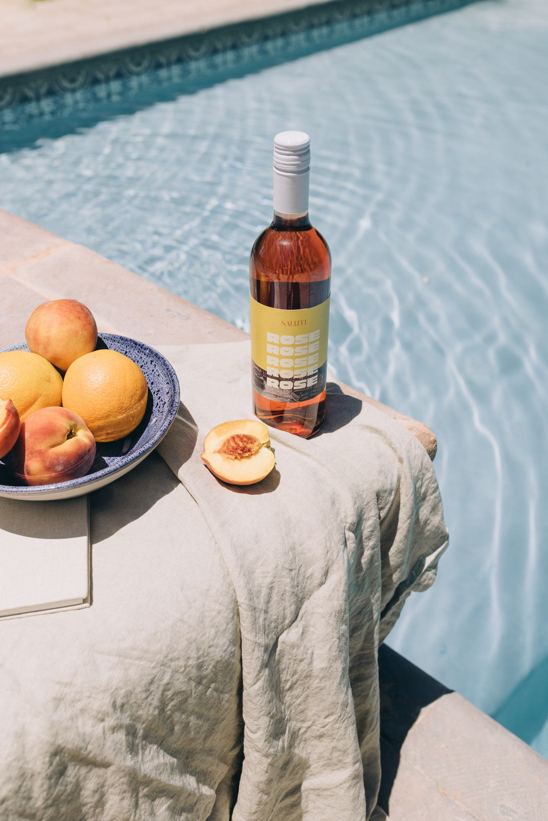 a bottle of wine and a bowl of fruits next to a pool