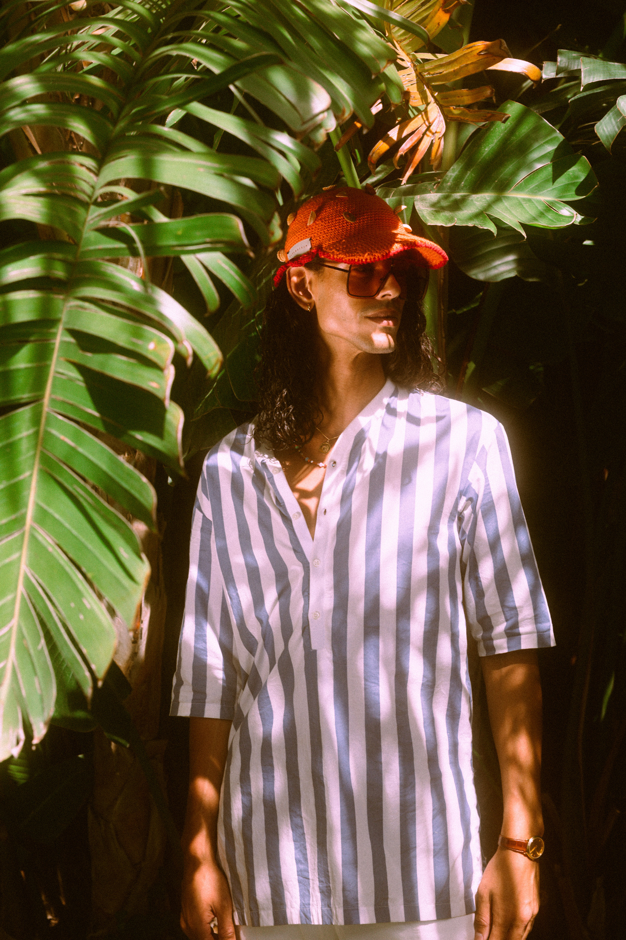 a person in a striped shirt and red hat standing in front of some plants